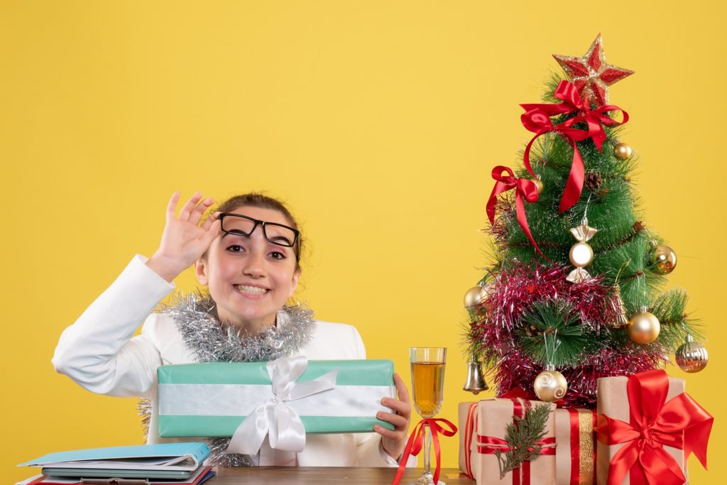 Woman with glasses opening up Christmas presents with a Christmas tree in the background
