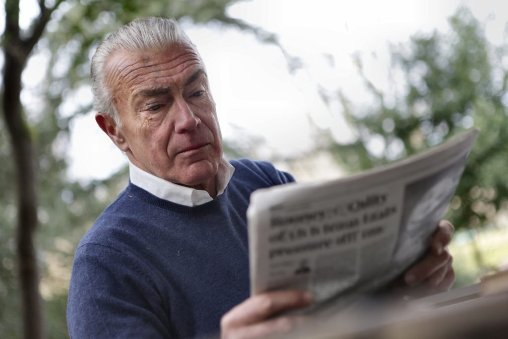 An older man with Presbyopia having difficulty reading a newspaper, while in a park