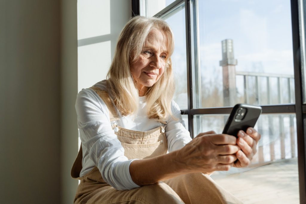 Older woman with presbyopia on her phone beside a window