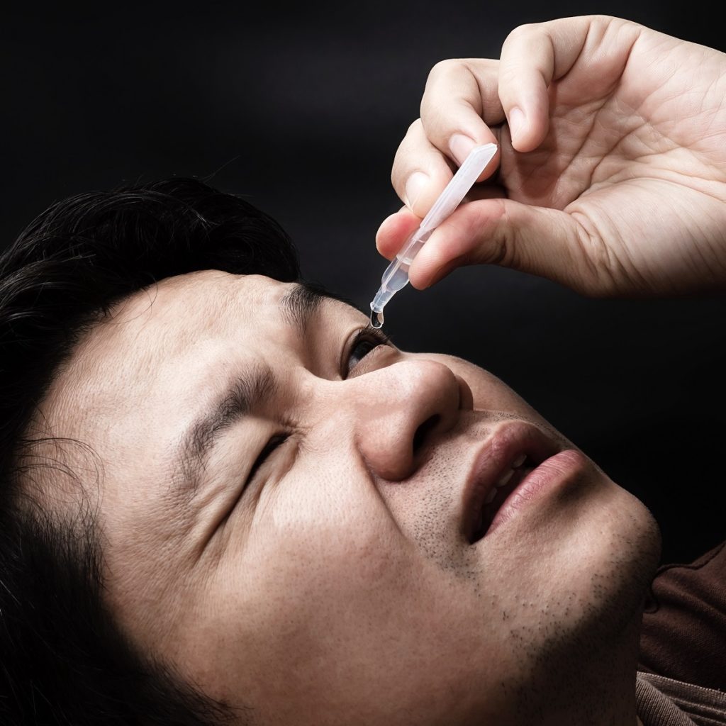 Man applying eye drops to relieve dry eye syndrome with black background