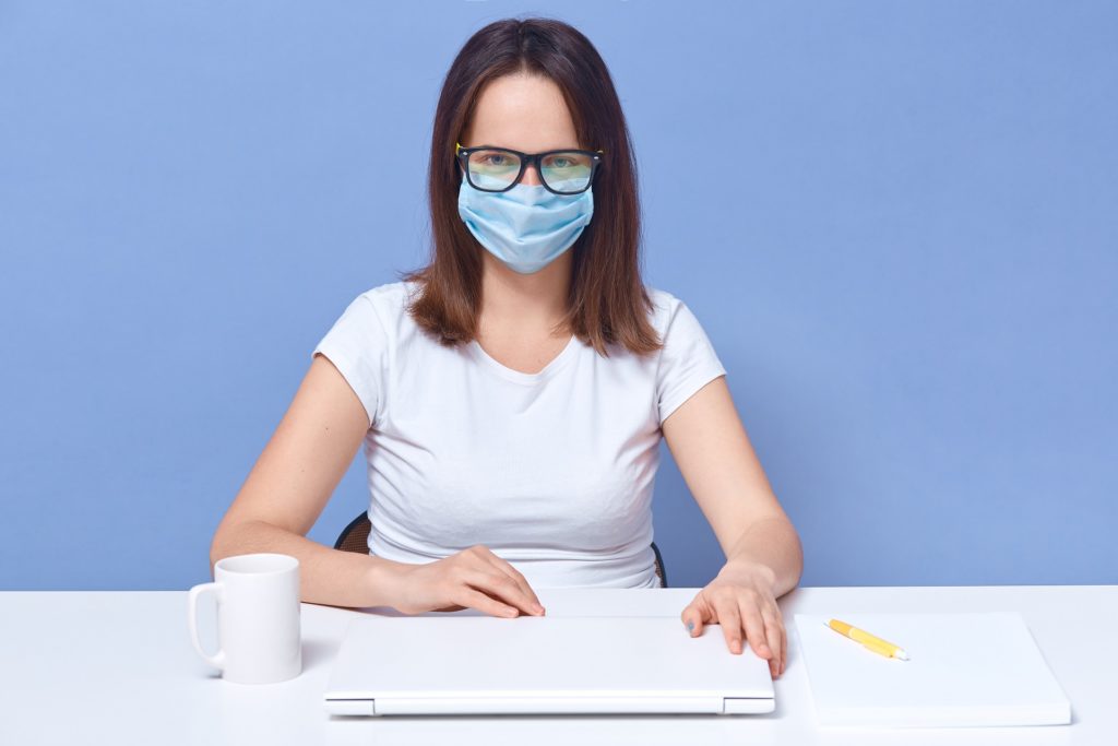 Woman wearing glasses and a face mask while working inside of her house